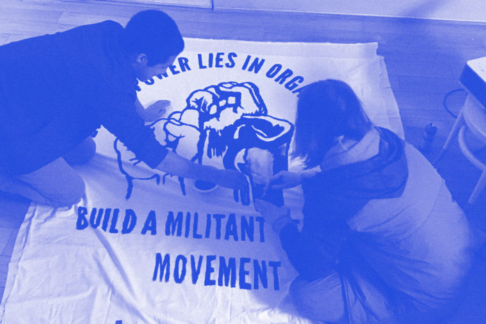 Photo of two individuals making banner with slogan "Our power lies in organization, build a militant tenant movement"