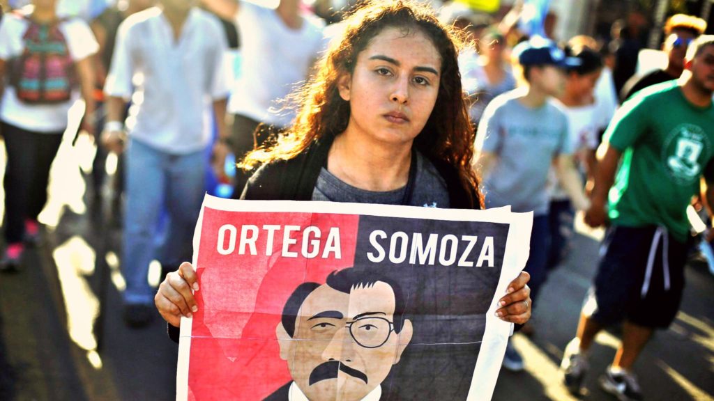 Image shows a woman carrying a sign during a protest than compares current president Ortega to Nicaraguan dictator Somoza