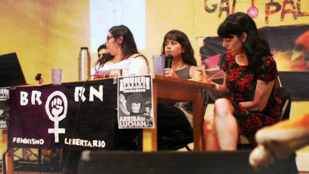 Three women sit behind a table giving a presentation.