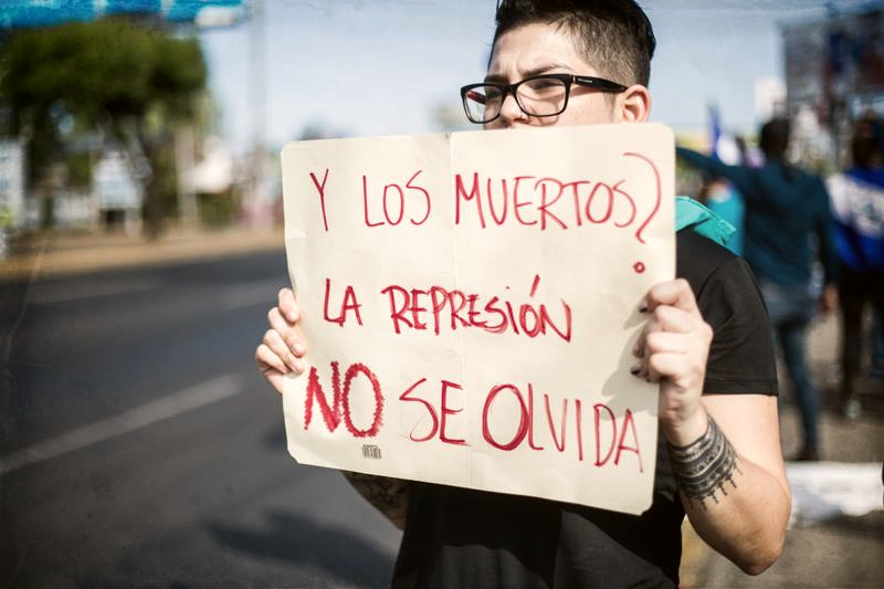 Young person holding sign "Y los muertos? La represion no se olvida / And the dead? We won't forget the [police] repression"