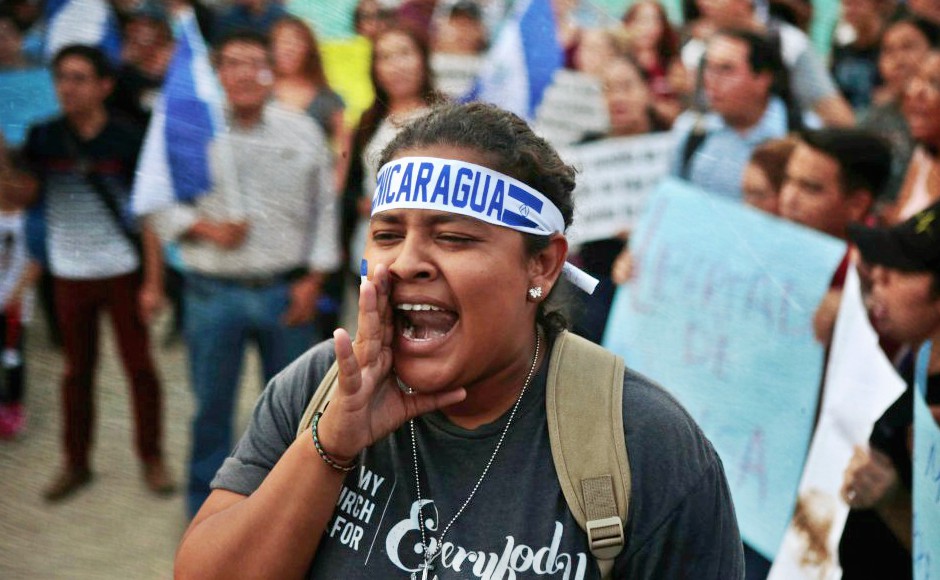 Woman leading chant with head band with blue text "Nicaragua"