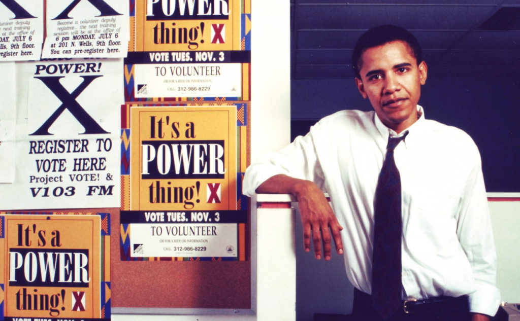 Photo of Barack Obama in his early years as a community organizer in Chicago. He is pictured next to pro-voting signs such as "It's a POWER thing! X"