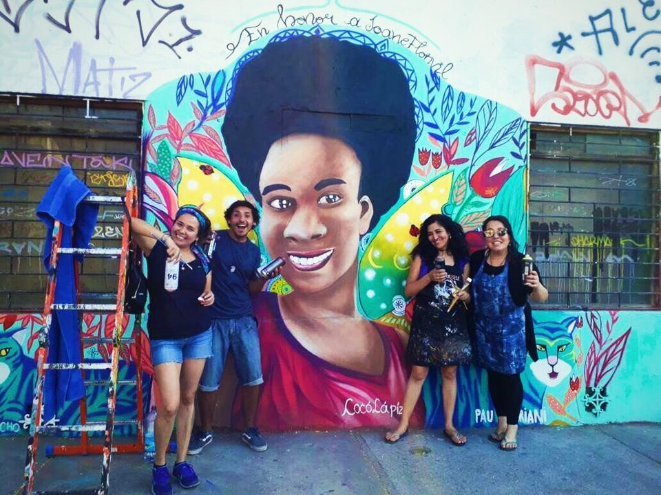 Four woman posed for picture in front of wall mural with painting tools in hand.