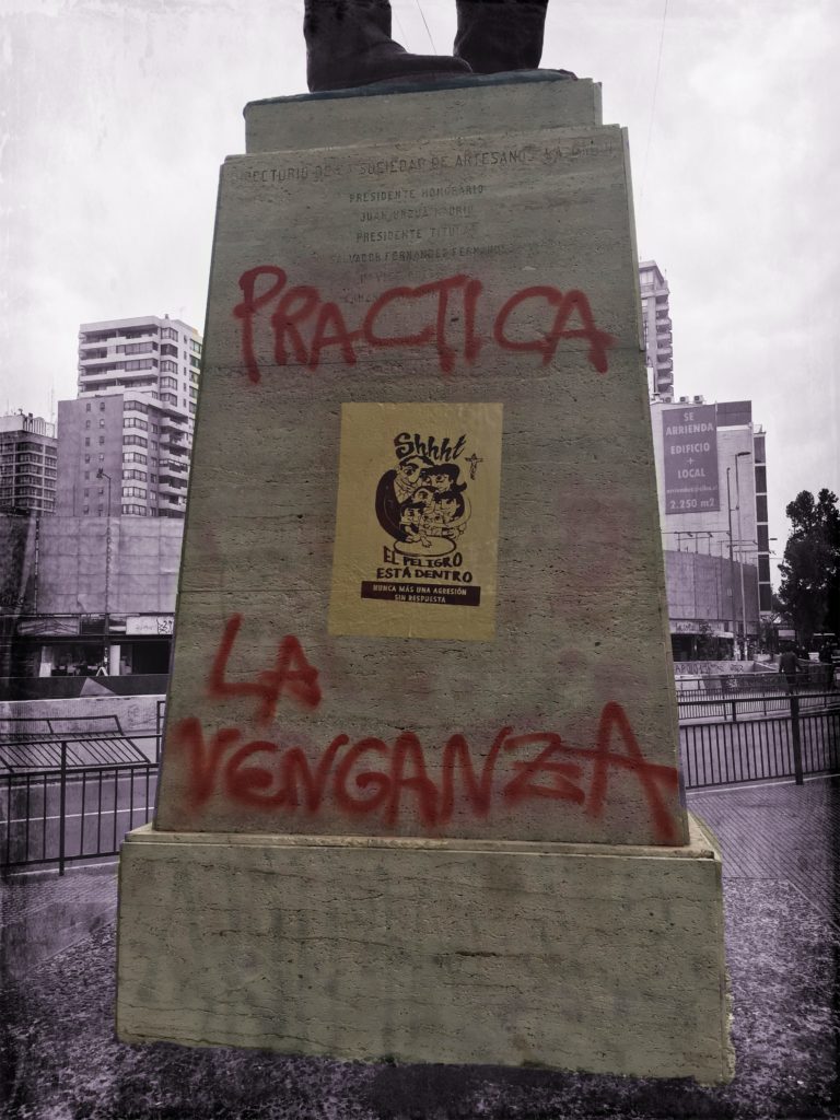 Statue in park with red graffiti and a wheat pasted poster.