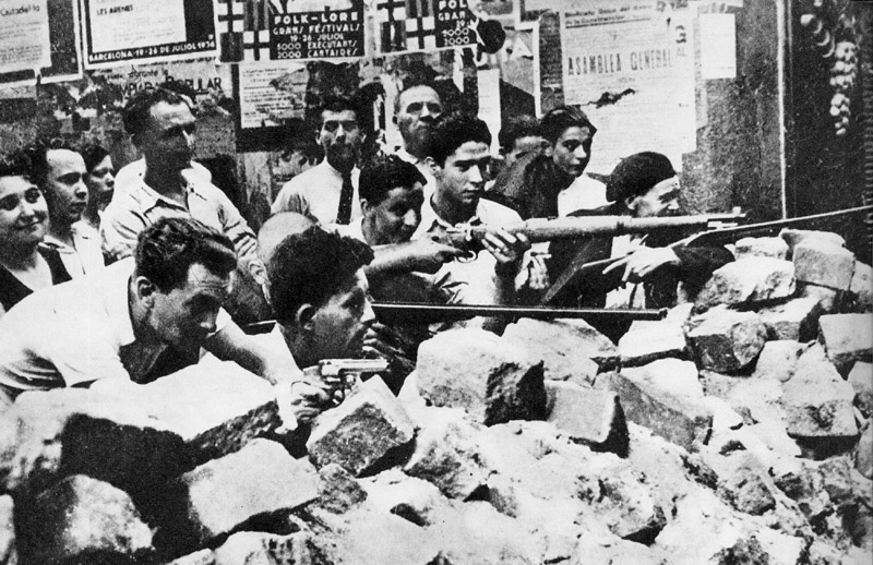 Photo of men lined up behind barricade of stones, guns at the ready.