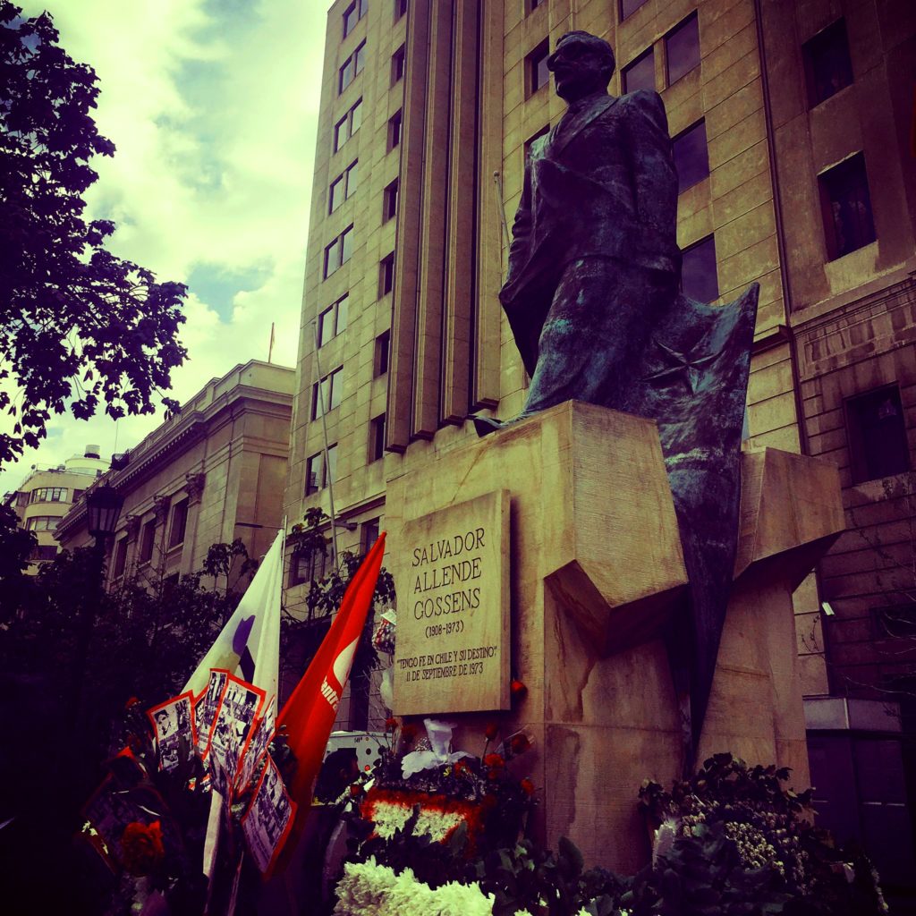 Photo of Allende Memorial statue with wreaths and flags surrounding the base. 