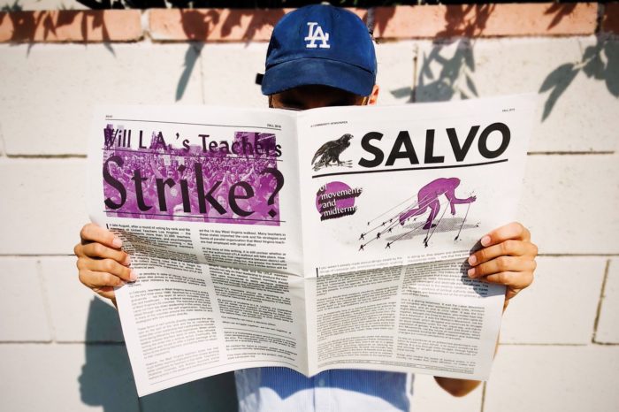 Photo of person wearing LA Dodgers hat holding and reading Salvo newspaper covering their face.