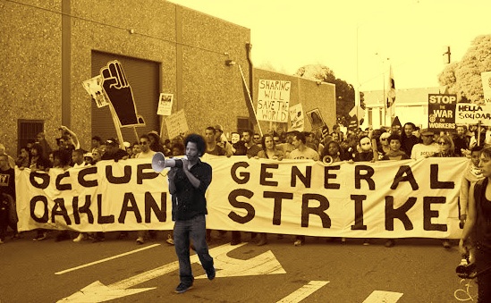 Photo of Boots Riley with bull horn in front of banner saying "occupy oakland, general strike"