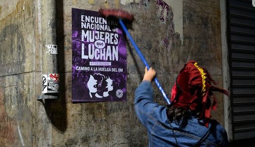 Woman facing away from camera holding brush as they affix a poster to a wall.