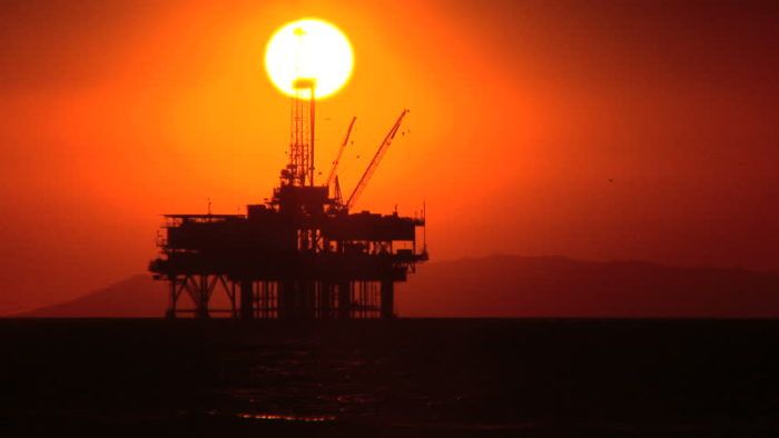 Ocean oil rig backed by a setting sun with a deep red sky. 