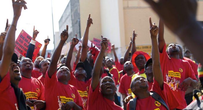 Rally of NUMSA union members, wearing red shirts pointing upwards.