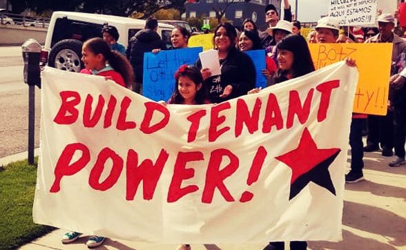 Photo of tenants in LA Chinatown protesting displacement and holding banner with "build tenant power!" with red and black star.