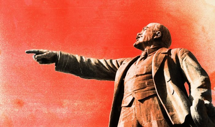Statue of Lenin pointing with red backdrop.
